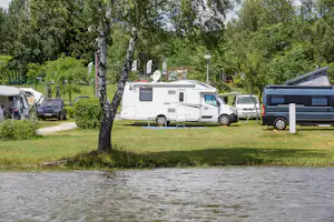Wohnmobile auf einem Campingplatz zwischen Bäumen, mit Rasenfläche und Stellplätzen neben einem Weg.