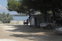 Autocamp Pisak - Stellplätze unter Bäumen mit dem Strand des Mittelmeeres im Hintergrund