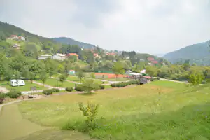Campinganlage im grünen Tal: Rasenflächen, Wege, Stellplätze mit Wohnmobil und kleine Gebäude am Hang.