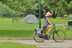 Fahrrad am Wegesrand, daneben Zelt auf dem Campingplatz im Grünen mit Stühlen und Bäumen im Hintergrund.