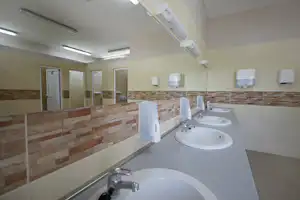 Camping-Badezimmer mit mehreren Waschbecken, Spiegeln, Seifenspendern und Handtuchhaltern an der gefliesten Wand.