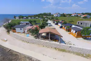 Campinganlage mit mehreren Mobilheimen, Holzverkleidung und Terrassen, Parkplatz mit Autos und Blick auf das Meer.