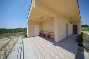 Überdachte Terrasse mit Küchenzeile am Ferienhaus, Fliesenboden, Geländer und Blick ins Grüne