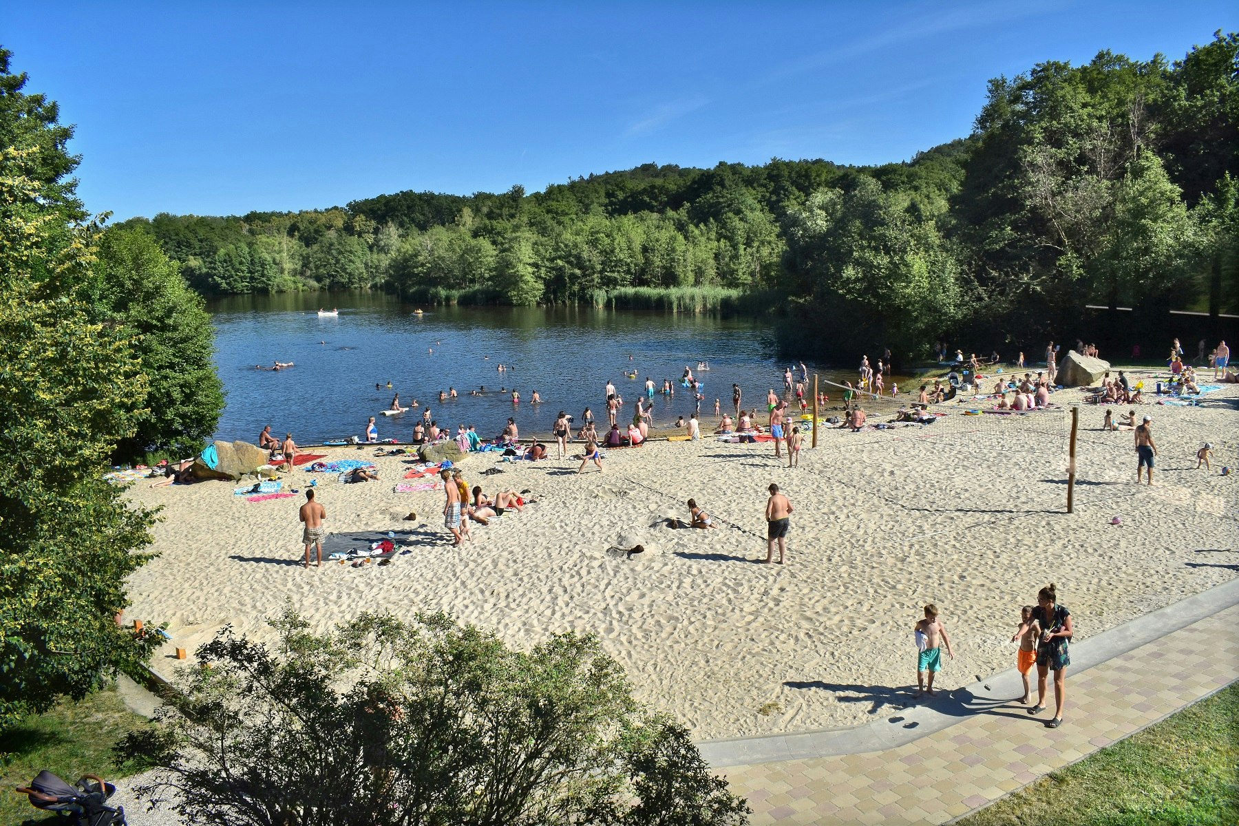 Autokamp Sedmihorky  - belebter Badestrand am See mit Volleyballfeld, der See ist umgeben von Wald