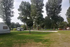 Wohnwagen und Wohnmobil auf einem Campingplatz-Stellplatz, mit Rasenfläche, Baumreihe und gepflegtem Weg im Hintergrund.