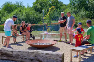 Familie spielt auf dem Campingplatz an einem Sandbereich mit Schaufeln, während Kinder und Erwachsene im Freien stehen.