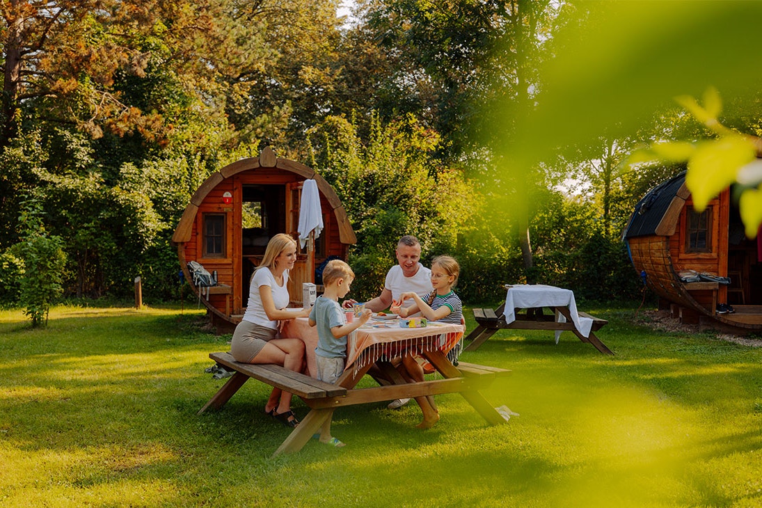 AZUR Campingpark Regensburg - Familie sitzt an einem Picknicktisch vor den Schlaffässern