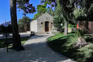 Steinernes Gebäude mit Eingang auf einem Campingplatz, gepflasterter Weg, Rasen und Bäume im Hintergrund.