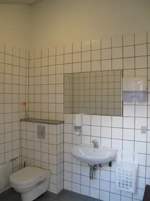 Badezimmer im Camping: Fliesenwand, Waschbecken mit Armatur, Spender und WC im Hintergrund.