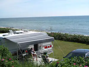 Wohnwagen mit Markise am Campingplatz, Blick auf das Meer, Blumenbeete am Ufer und ein paar Stege im Wasser.