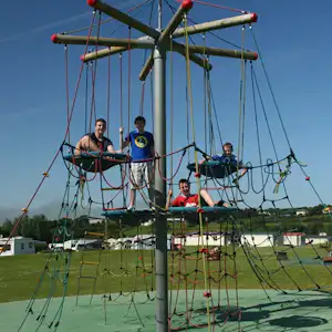 Spielplatz mit Kletter- und Seilnetz am Campingplatz, im Hintergrund Zelte und Wohnwagen auf einer Wiese.