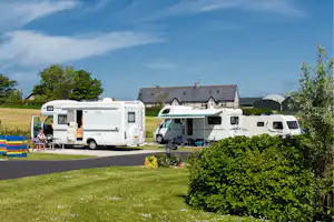 Wohnmobile auf einem Campingplatz-Stellplatz, mit geöffnetem Fahrzeug, Gartenweg und Wohngebäude im Hintergrund.