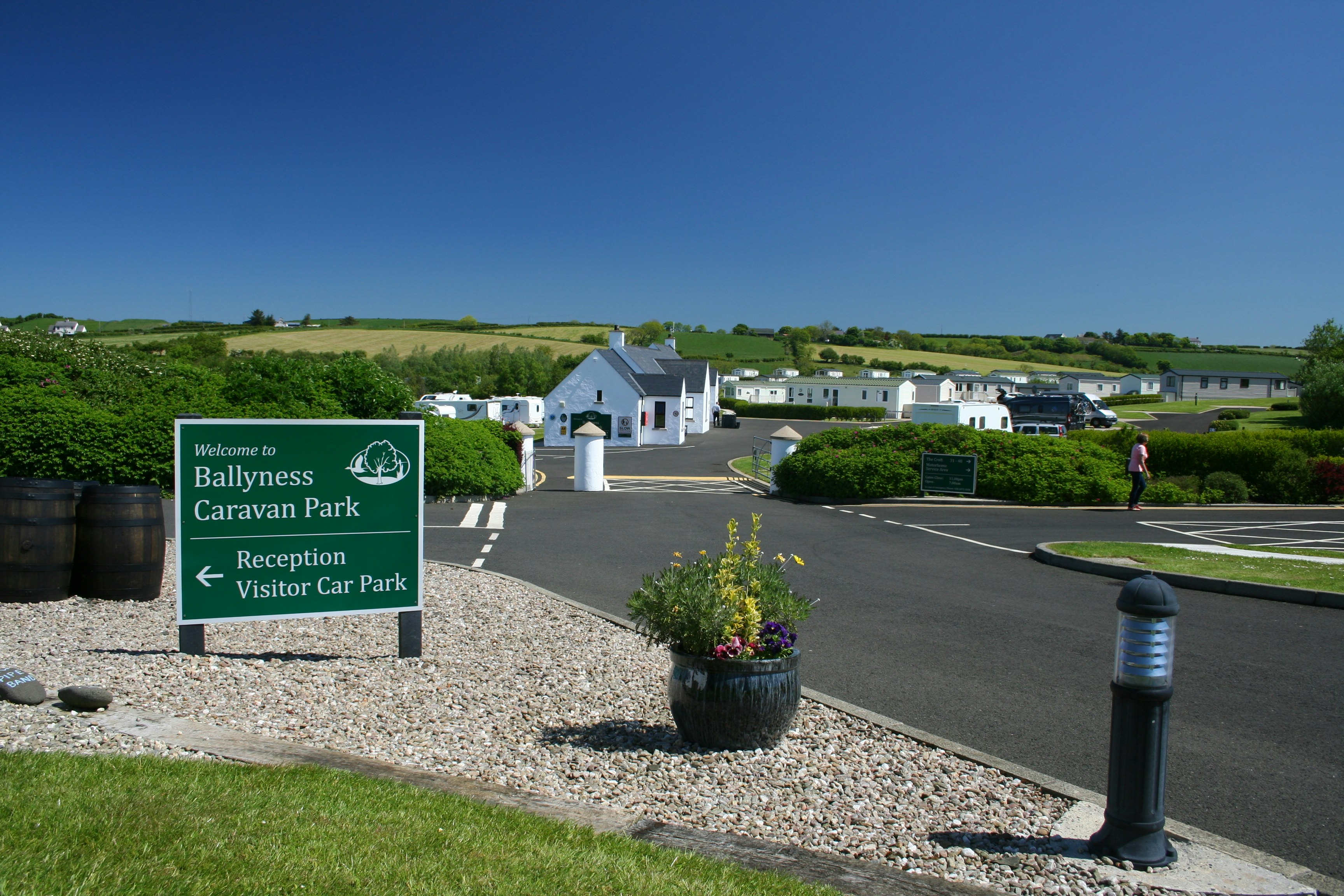 Schild „Welcome to Ballyness Caravan Park“ am Eingang, mit Rezeption, Parkplatz und Wohnwagen auf dem Campinggelände.