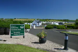 Schild „Welcome to Ballyness Caravan Park“ am Eingang, mit Rezeption, Parkplatz und Wohnwagen auf dem Campinggelände.