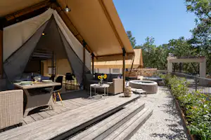 Großes Campingzelt auf einer Holzterrasse mit Sitzgruppe, Tisch und Pflanzen im Gartenbereich.