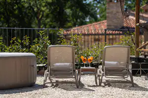 Zwei Campingstühle auf einer Kiesfläche vor einem Gartenzaun, daneben ein Sitzsack und ein kleiner Tisch mit Blumen.