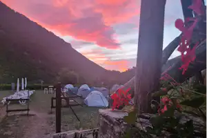 Campingzelte im Tal, Berge im Hintergrund und ein farbiger Sonnenuntergang am Himmel.