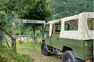 Militärfahrzeug mit Zeltaufbau am Campingplatz, Schild „BASE CAMP 1070“ und Weg am Zaun im Grünen.