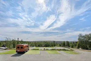 Wohnmobil auf einem Campingplatz mit Rasenflächen und Wegen, im Hintergrund Bäume, Felder und eine weite Landschaft.