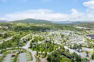Luftaufnahme eines Campingplatzes mit vielen Stellplätzen, Wohnwagen und Zelten, umgeben von Wäldern und Hügeln.