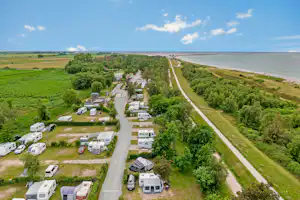 Campingplatz mit Wohnmobilen und Stellplätzen, Feldweg zum Meer, grüne Landschaft und Bäume am Ufer.