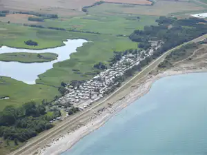 Luftaufnahme eines Campingplatzes am Fluss und See mit vielen Wohnwagen, Zufahrtsstraße und Ufer am Wasser.