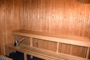 Holzbank in einer Sauna mit Wasserbehälter und Holzpaneelen an der Wand, Detailaufnahme im Innenraum.