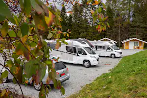 Wohnmobile auf einem Campingplatz-Stellplatz, Kiesweg und Rasenfläche, im Hintergrund kleine Gebäude und Bäume.