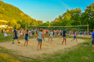 Strandvolleyballfeld auf dem Campingplatz mit Netz, Sand und vielen spielenden Kindern vor grünen Hügeln.