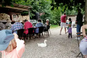 Gruppe sitzt an Campingstühlen im Garten, neben Holzunterstand und Stapel Brennholz, im Hintergrund Bäume und Hecke.