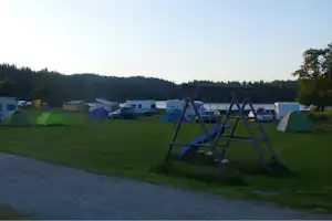 Zeltwiese auf dem Campingplatz mit bunten Zelten, Wohnmobilen und einem Spielgerät mit Schaukel im Vordergrund.