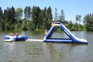 Auf dem See treiben zwei aufblasbare Boote, im Hintergrund hohe Bäume und ein Ufer am Campingplatz.