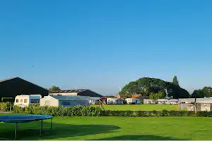 Zelt und Wohnwagen auf einem grünen Campingplatz, im Hintergrund Gebäude und Bäume.