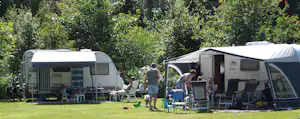 Zwei Wohnwagen auf einem Campingplatz mit Rasen, Sonnenschirmen und Stühlen vor den Eingängen, umgeben von Bäumen.