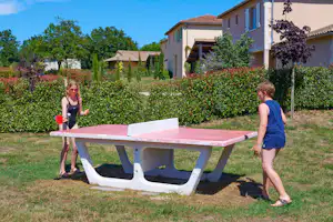 Spiel- und Tischtennisplatte auf dem Rasen vor Wohngebäuden, Hecken und Bäumen auf dem Campingplatz.