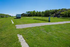 Wohnmobil auf einem Stellplatz auf grünem Rasen, mit Betonwegen, Bäumen und Hecken im Hintergrund.