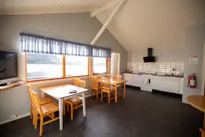 Innenansicht eines Wohnwagens mit Essbereich und Holztisch, daneben Küchenzeile mit Herd und Spüle, große Fensterfront.