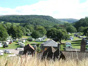 Campingplatz im Tal mit Wohnwagen und Zelten, Blick auf Holzgebäude, gepflegte Wiesen und Bäume.