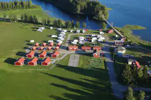 Luftaufnahme eines Campingplatzes am Fluss mit Reihen von Ferienhäusern, Stellplätzen, Wegen und Grünflächen am Ufer.