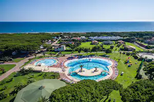 Luftaufnahme einer Campinganlage mit zwei großen Schwimmbecken, Liegen, Wegen und Grünflächen nahe dem Meer.