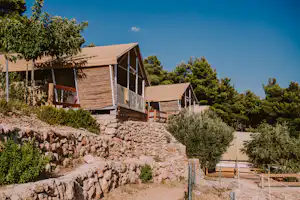 Holz-Bungalows auf einem Hang mit Steinmauer, Bäumen und Wegen, im Hintergrund weitere Unterkünfte.