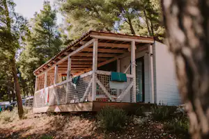 Holzveranda an einer Camping-Unterkunft im Wald, mit Sichtschutz, Wäscheleine und seitlicher Tür am Gebäude.