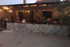 Terrasse mit Steinmauer und warmen Lichtern, mehrere Personen sitzen am Tisch vor einem Gebäude.