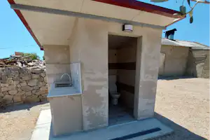 Außenküche mit Grillbereich unter einem Vordach, Steinmauer im Hintergrund und Kiesboden am Campingplatz.