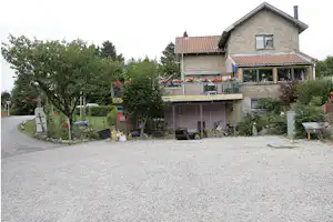 Ferienhaus mit Terrasse, Balkon und Garten; Kiesweg vor dem Gebäude, Bäume und Sträucher im Hintergrund.