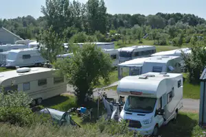 Reihe von Wohnmobilen und Caravans auf einem Campingplatz, umgeben von Bäumen und Rasen.