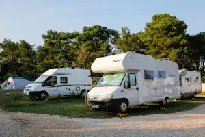 Wohnmobile auf einem Campingplatz, im Vordergrund ein weißes Wohnmobil mit Markise, im Hintergrund weitere Fahrzeuge und Bäume.