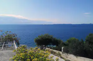 Blick vom Campingplatz auf das Meer, mit Terrasse, Geländer und Büschen im Vordergrund.