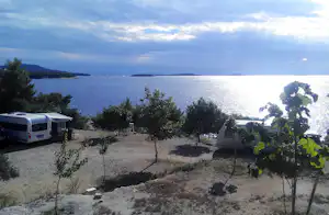 Wohnwagen und Zelte auf einem Campingplatz am See, mit Bäumen und Weg zum Ufer, Blick über das Wasser.