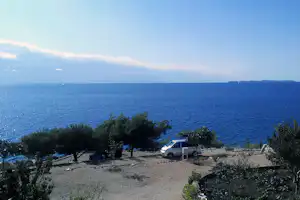 Blick vom Campingplatz auf das Meer, Stellplätze mit Wohnwagen und Bäumen im Vordergrund.